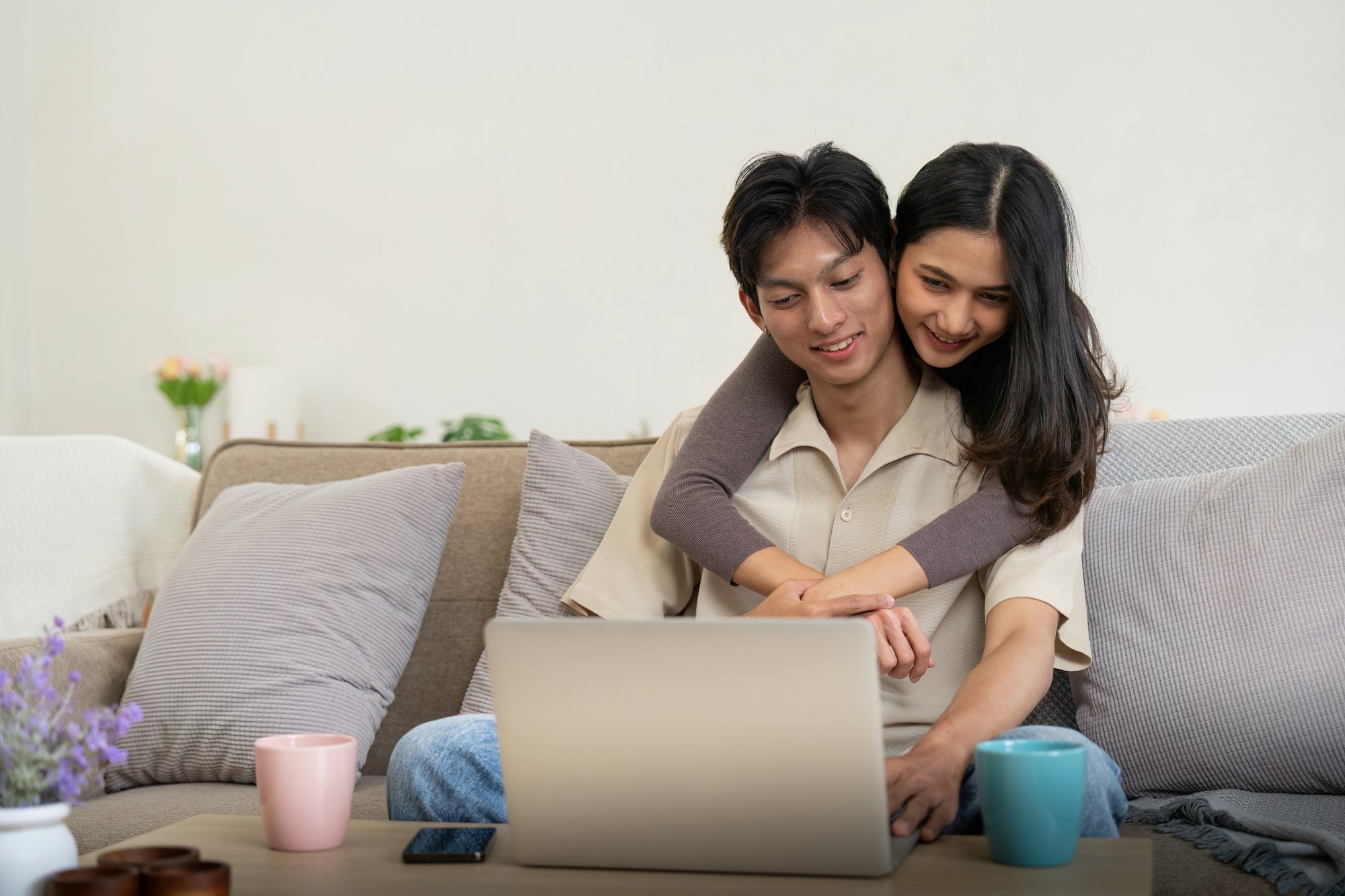 Young couple asian using laptop together while sitting on sofa at home